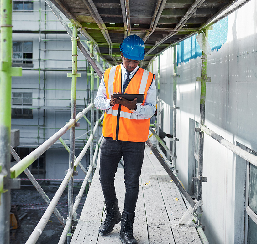 A man with a hardhat and safety vest walking on scaffolding - Pavion Fire Safety, Integration, and Security