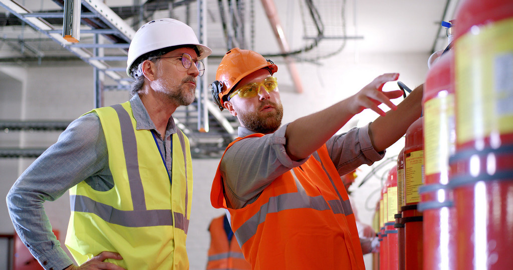 Bearded worker demonstrating fire extinguishers to mature inspector while working on power station